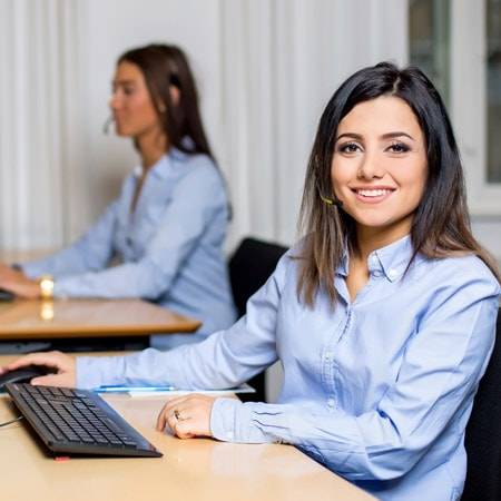 telefonpasning, medarbejder ved arbejdsstation med headset på smiler til kameraet